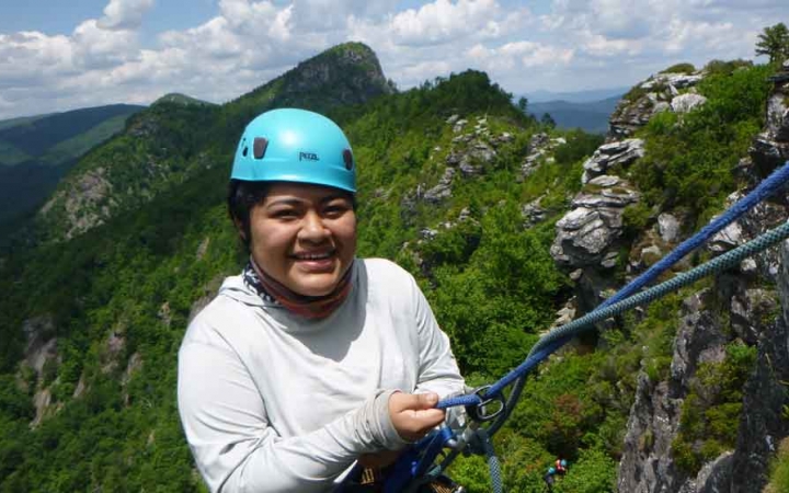a high school student who is rock climbing smiles at the camera on an outward bound trip in north carolina